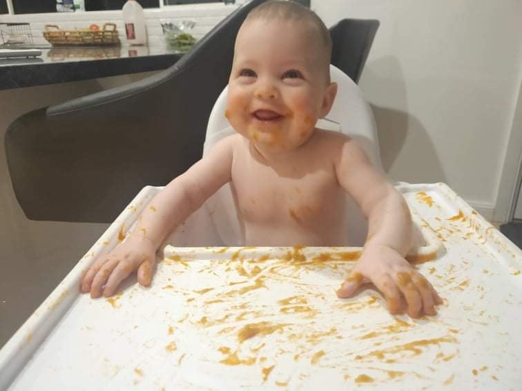 baby girl in high chair with no safety straps on and messy food everywhere